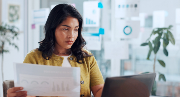 Image of a woman looking at her computer with a piece of paper in her hand