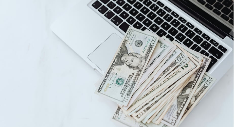 Image of a computer on a desk with cash spread out on the keyboard